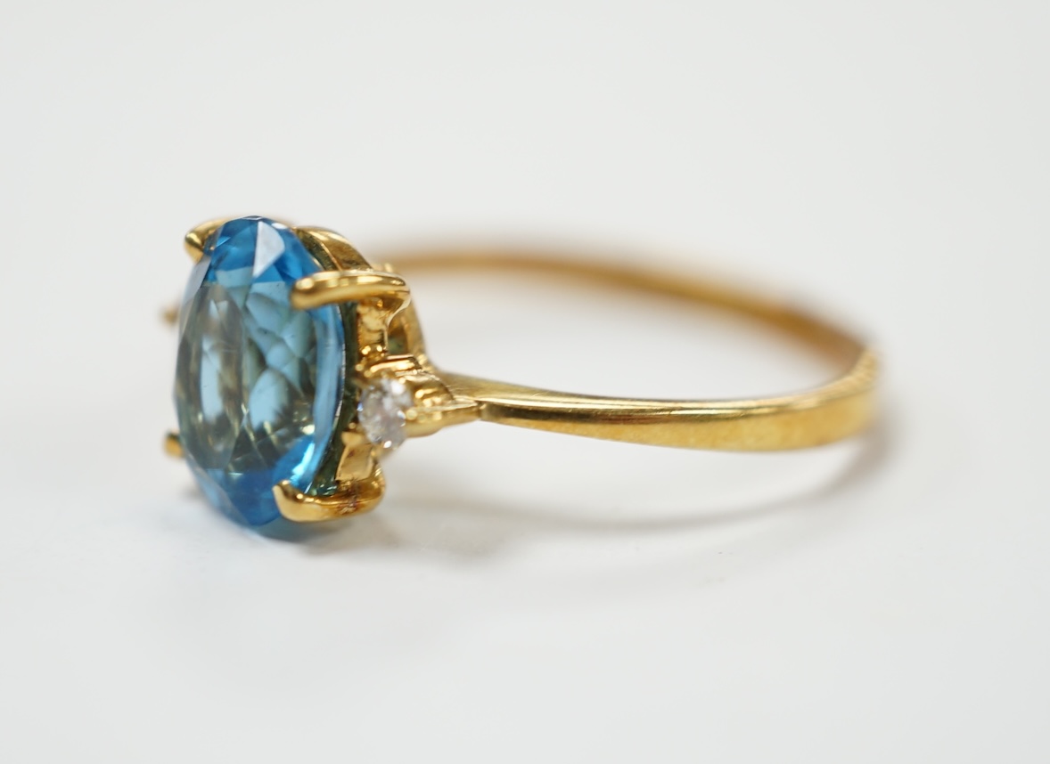A 750 yellow metal and single stone oval cut blue topaz and two stone diamond set ring, size M/N, gross weight 2.5 grams. Good condition.